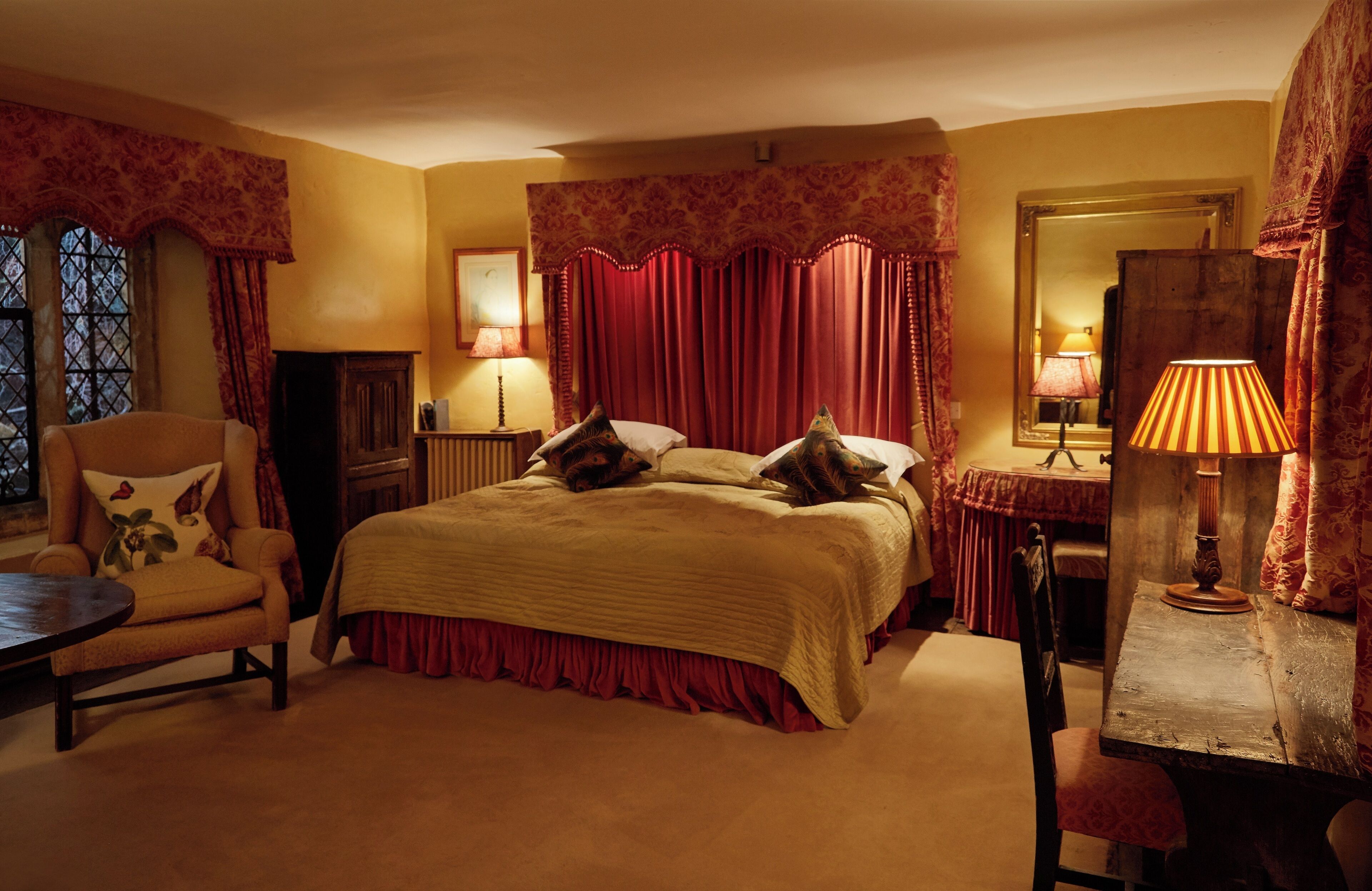 A bedroom with a large bed, two bedside tables, a chair, a small table, and a mirror.