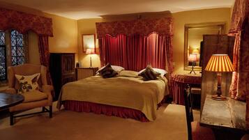 A bedroom with a large bed, two bedside tables, a chair, a small table, and a mirror.
