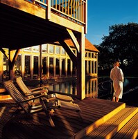 Um deck de madeira com espreguiçadeiras e área de piscina, com vista para um corpo d'água.