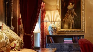 A bedroom with a bed, a nightstand with books, a lamp, a vase, and a framed portrait on the wall.