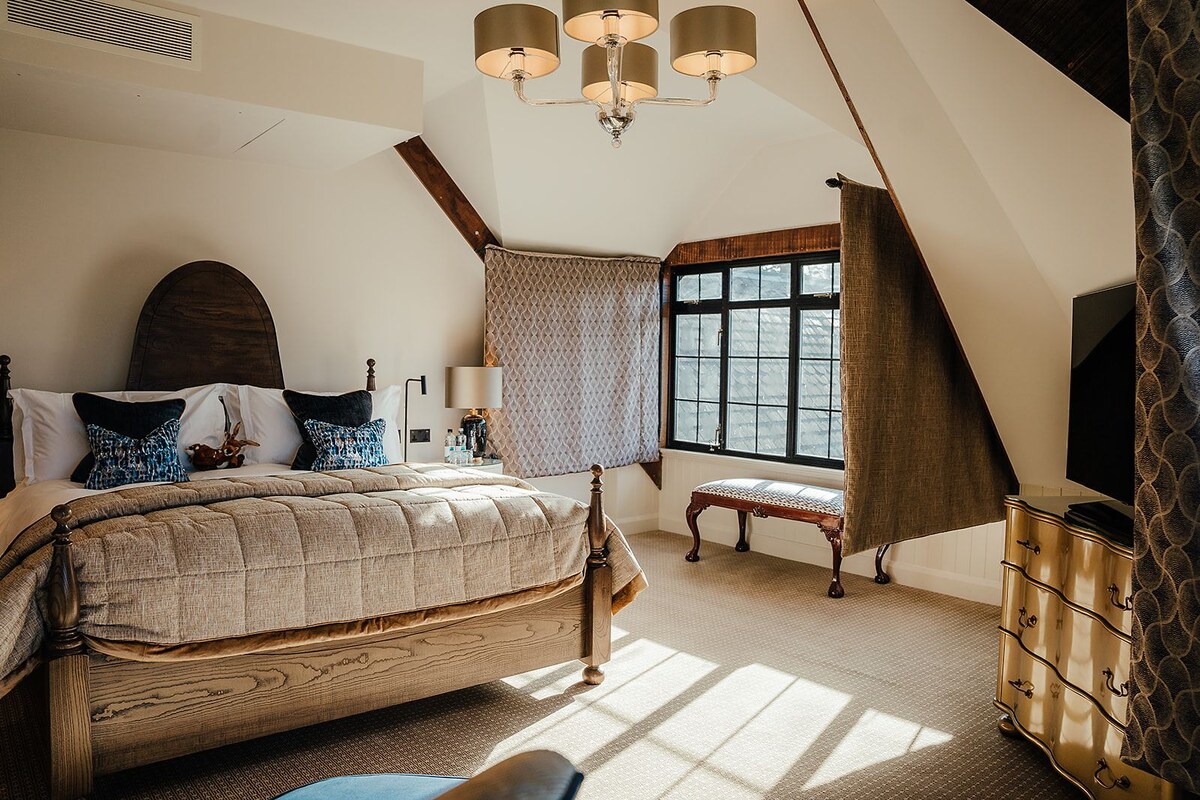 Un dormitorio con una cama grande, un banco de madera, un aparador y una ventana con cortinas.