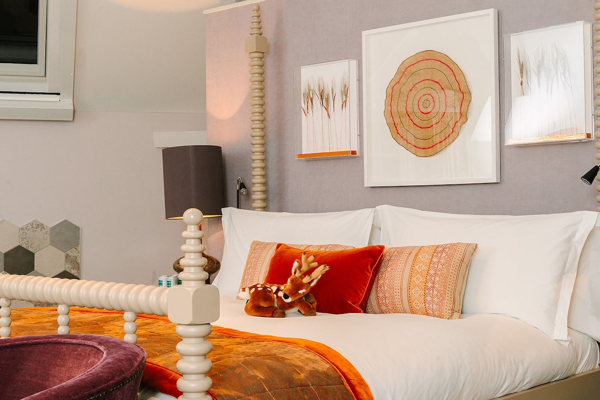Un dormitorio con cama, cabecera, mesita de noche, lámpara y decoración en la pared.