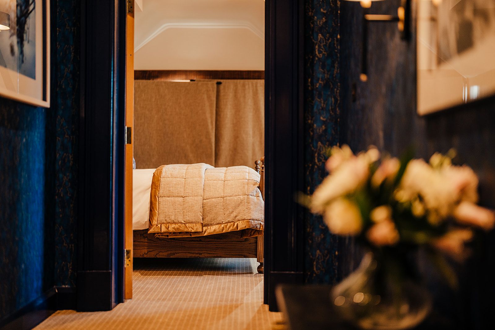Una habitación de hotel con una cama, un florero con flores y vistas a otra habitación.