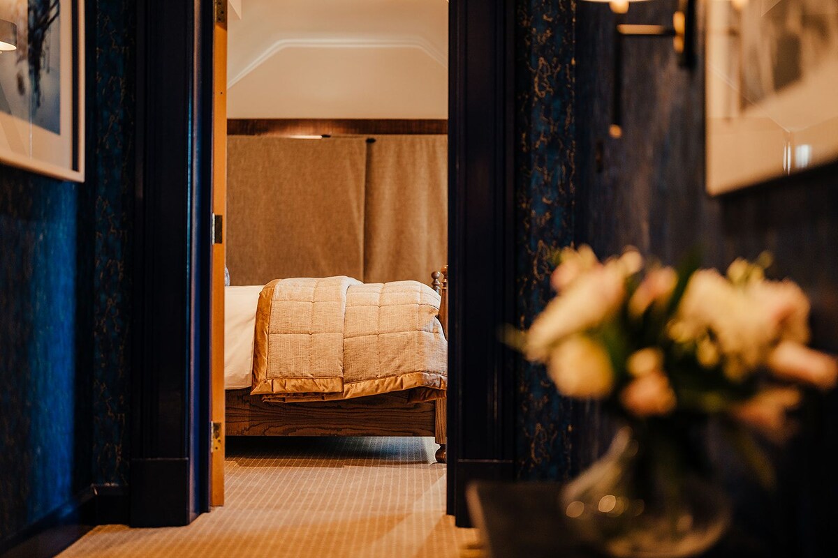 A hotel room with a bed, a vase with flowers, and a view of another room.
