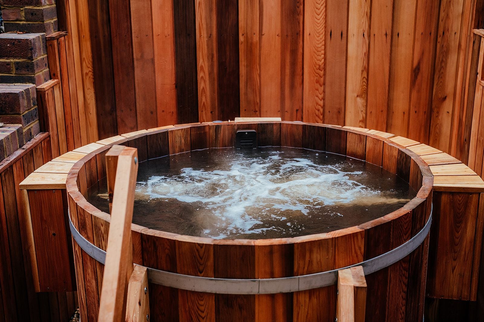 Jacuzzi circular con exterior de madera y estructura metálica, rodeado de paredes de madera.