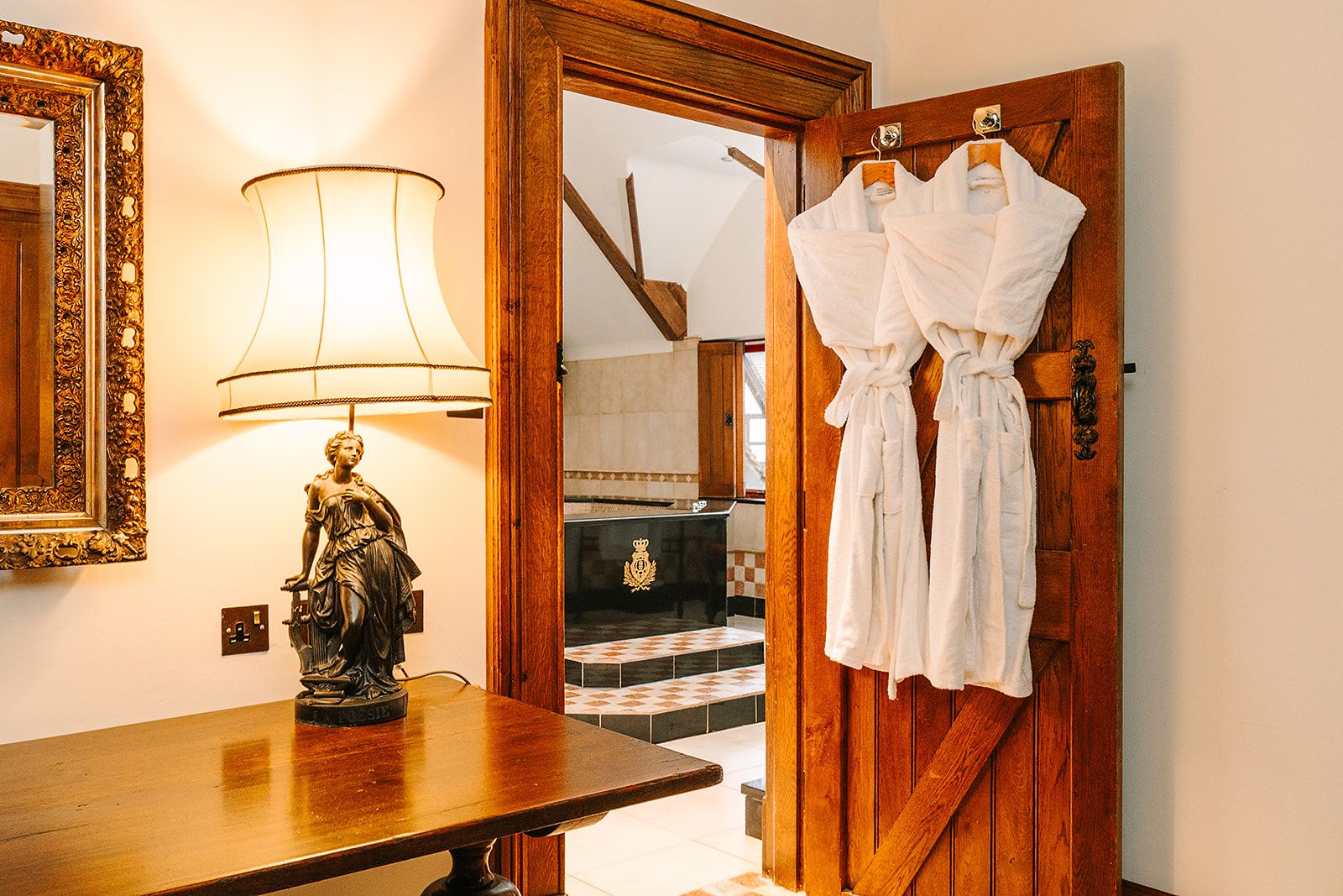 A wooden door with two white robes hanging on hooks, a statue on a table, and a lamp with a white shade.