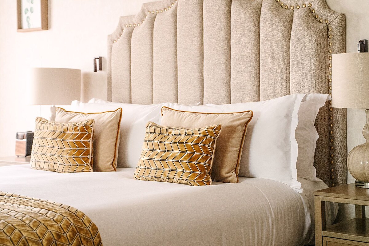 A bed with a tufted headboard, two patterned pillows, and a bedside table with a lamp.