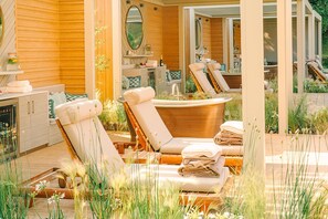 A spa area with two lounge chairs, a bathtub, and a wooden deck surrounded by plants. - Pennyhill Park (Bagshot)