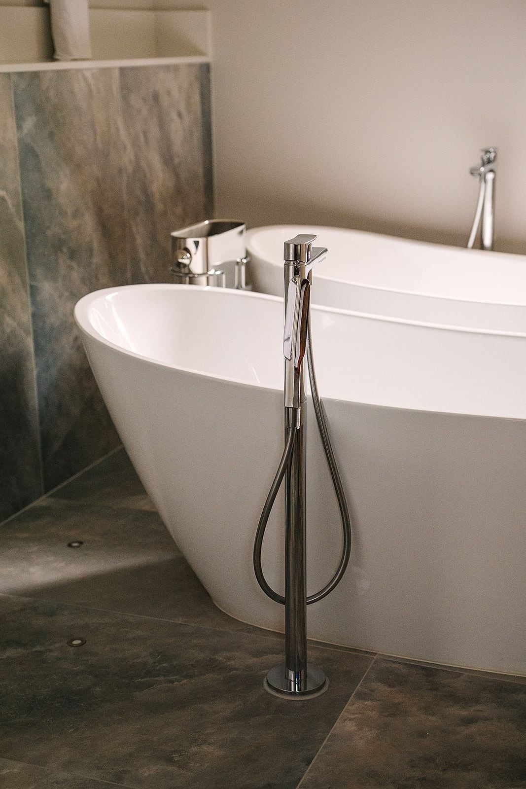 A modern bathroom with a freestanding bathtub, a handheld showerhead, and a separate faucet.