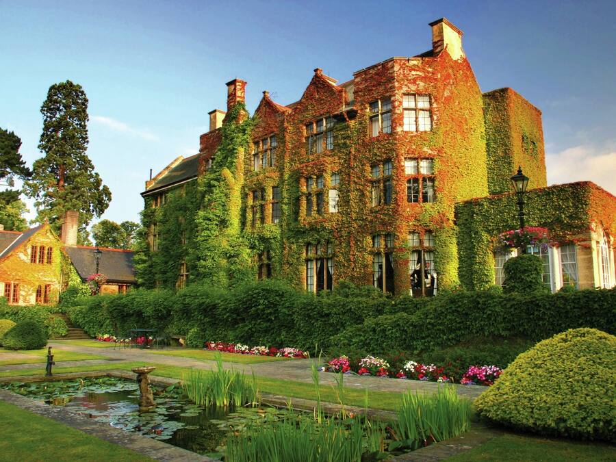A large ivy-covered building with a formal garden, including a pond and well-manicured lawns.