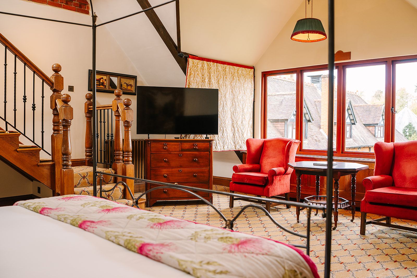 Un dormitorio con cama, televisor, cómoda, silla, mesa y ventana con vista a edificios.