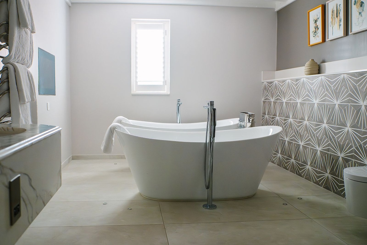 A modern bathroom with a freestanding bathtub, a window, and a geometric patterned wall.