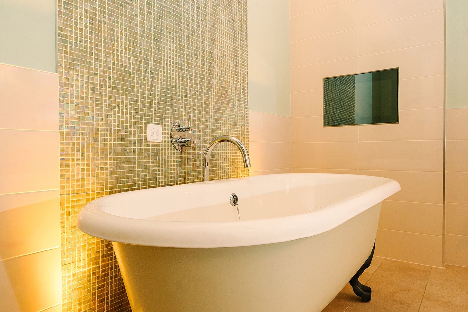 A bathroom with a freestanding bathtub, a tiled wall, and a small mirror.
