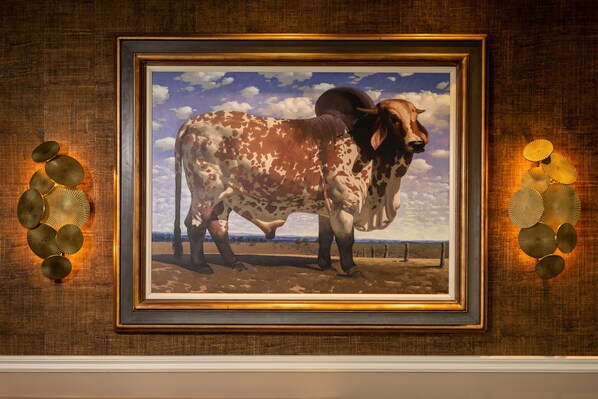 A framed painting of a cow on a fence with a clear sky in the background.