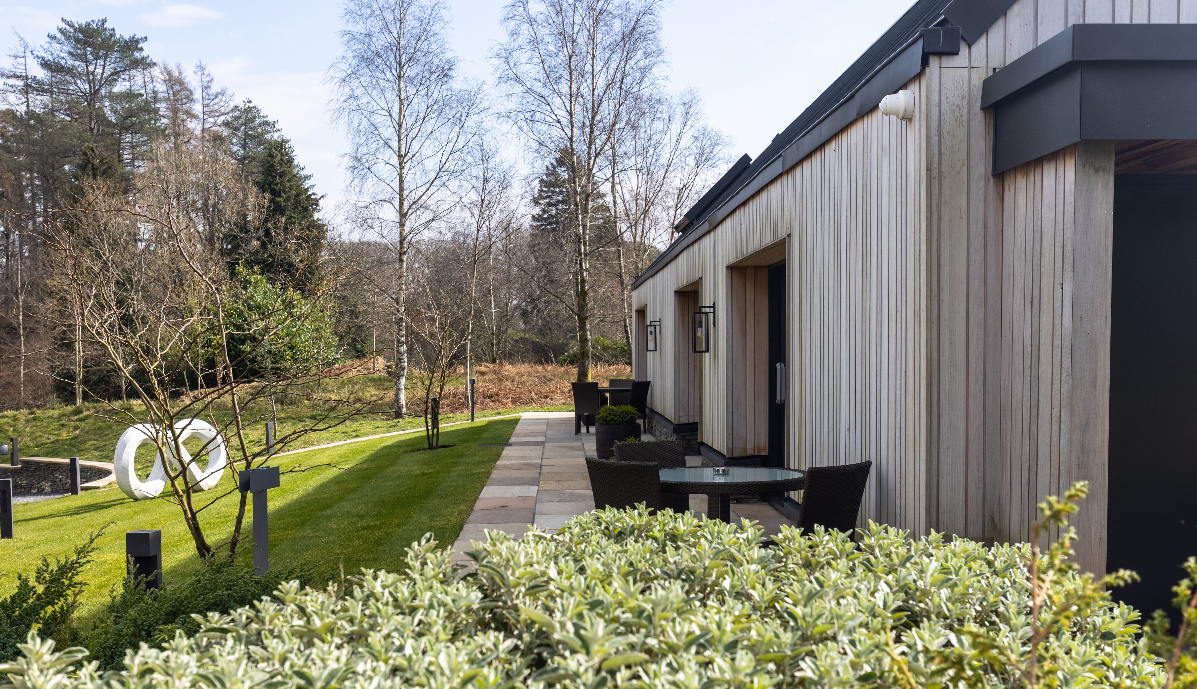 Een modern gebouw met een terras, buitenzitplaatsen en een verzorgde tuin.