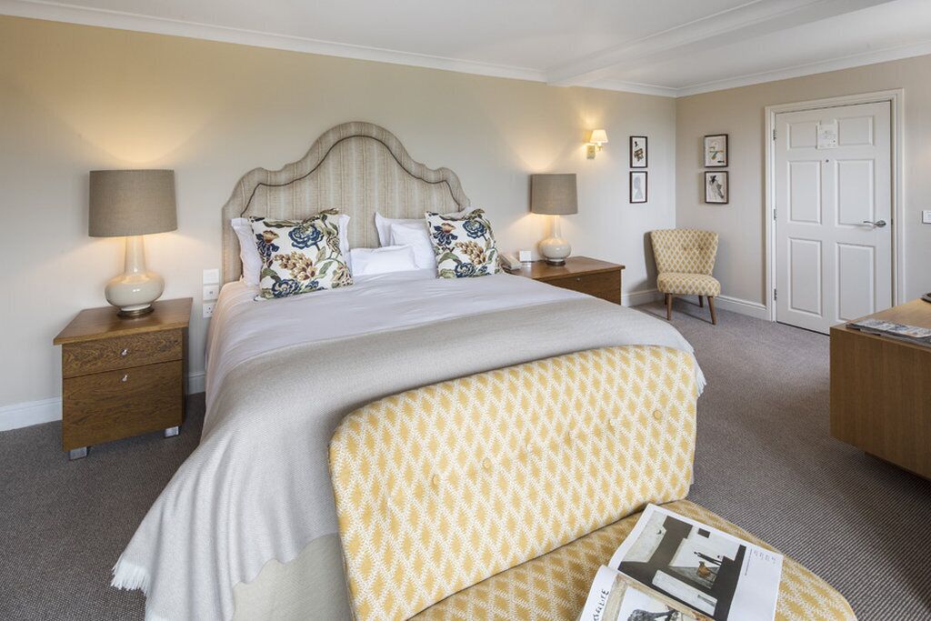 A neatly arranged hotel room with a large bed, two bedside tables, a chair, a desk, and a door.