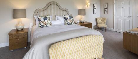 A neatly arranged hotel room with a large bed, two bedside tables, a chair, a desk, and a door.