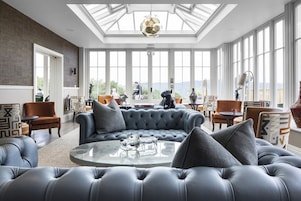 A spacious living room with a large sectional sofa, a glass coffee table, and a high ceiling with skylights.