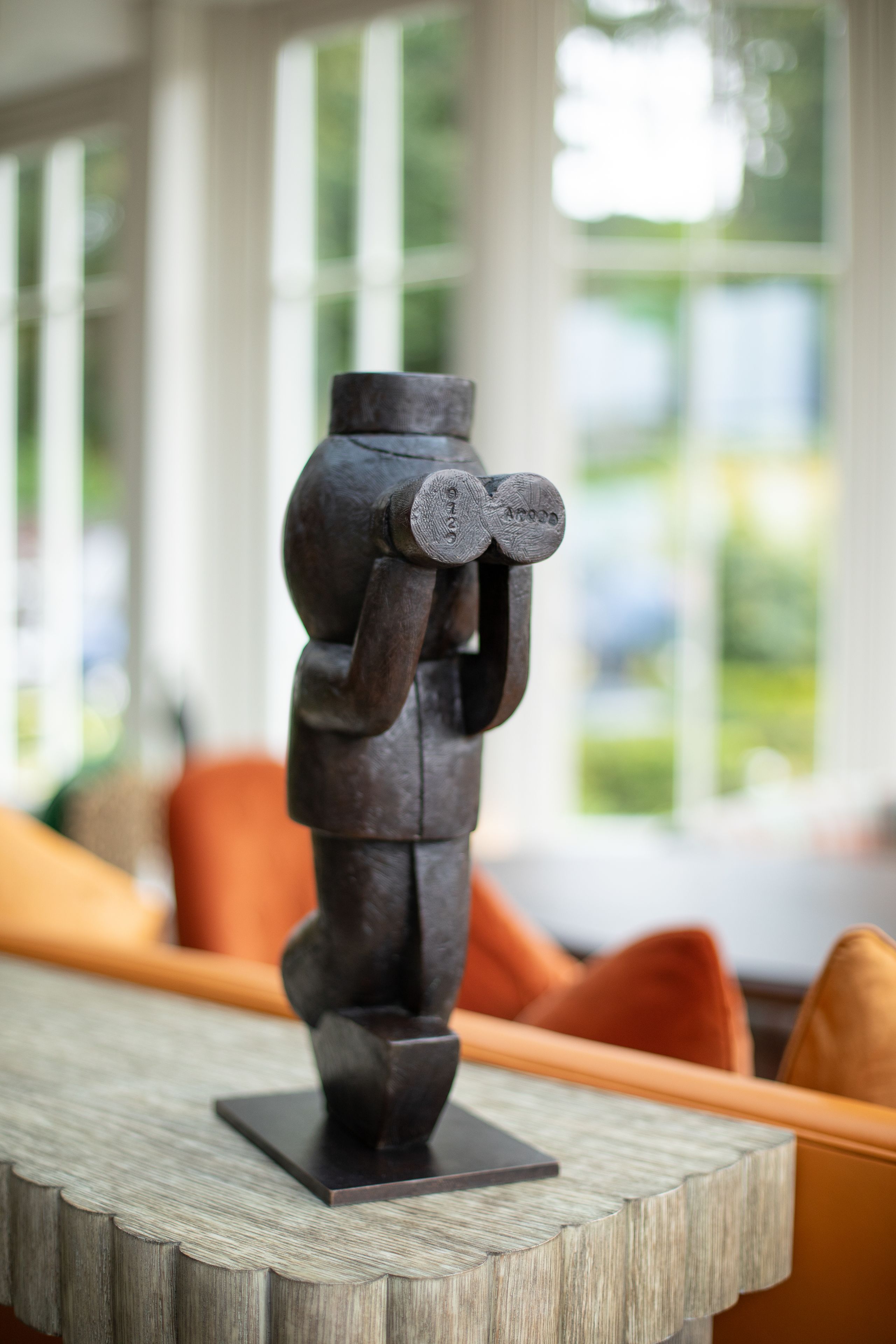 Een sculptuur op een houten tafel in een kamer met uitzicht op groen door grote ramen.