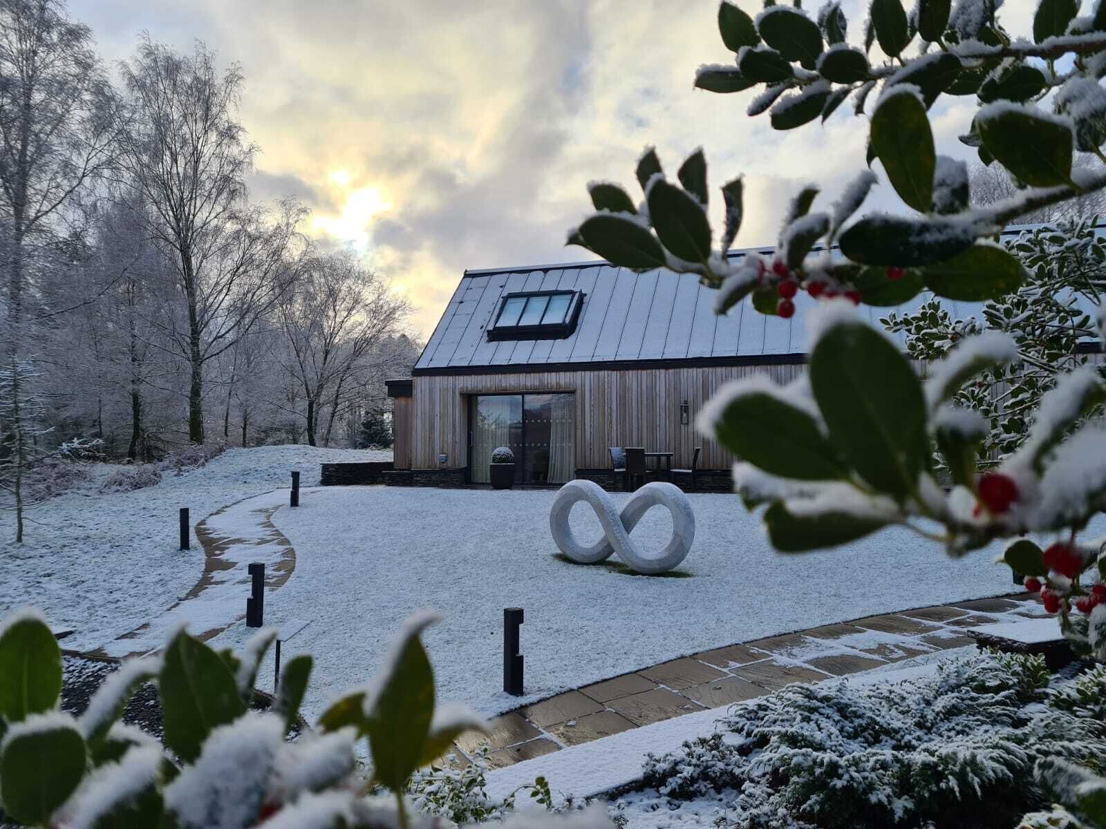 A modern building with a sloped roof and large windows, surrounded by snow-covered ground and trees.