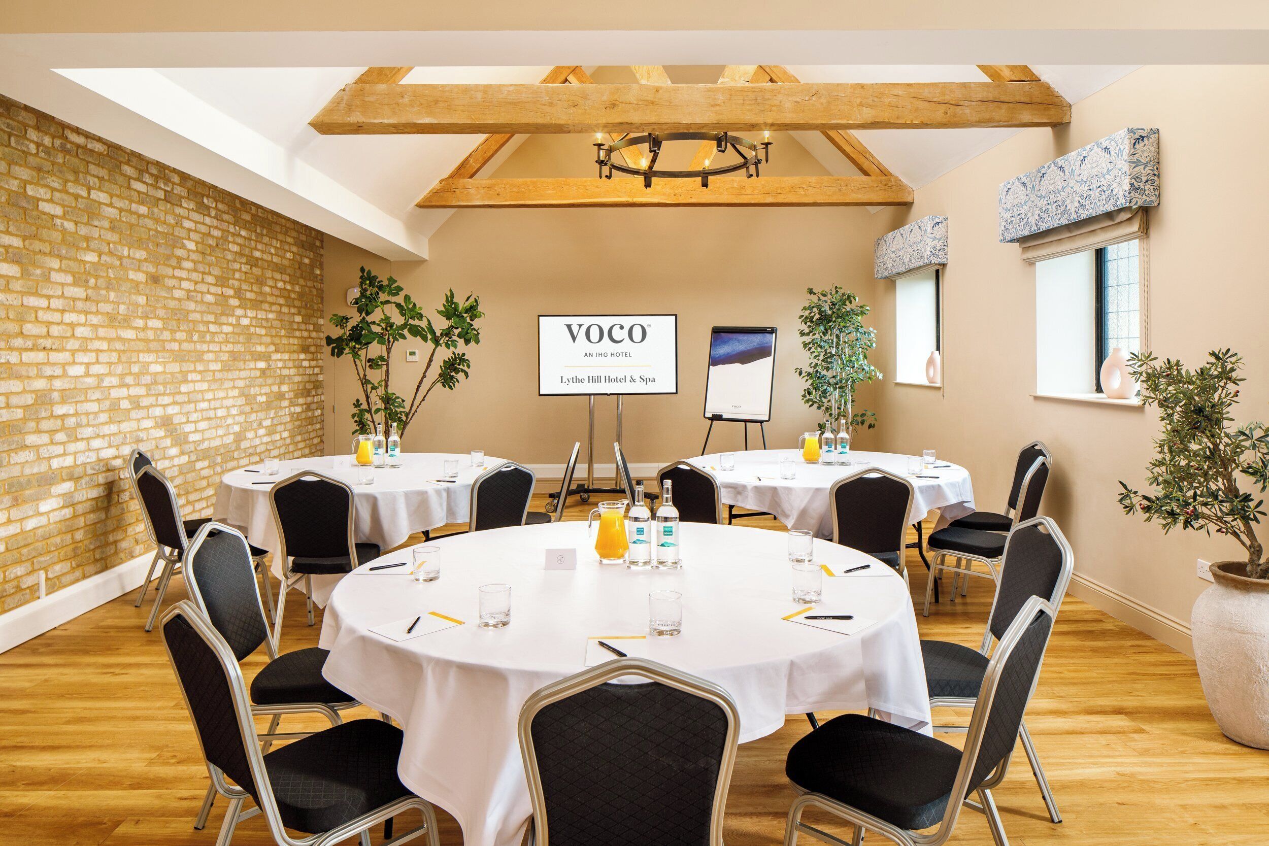 Ein Konferenzraum mit runden Tischen, Stühlen und einem Schild mit der Aufschrift 'Voco An IHG Hotel'.