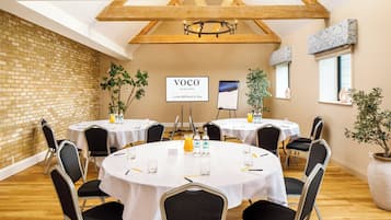 Ein Konferenzraum mit runden Tischen, Stühlen und einem Schild mit der Aufschrift 'Voco An IHG Hotel'.