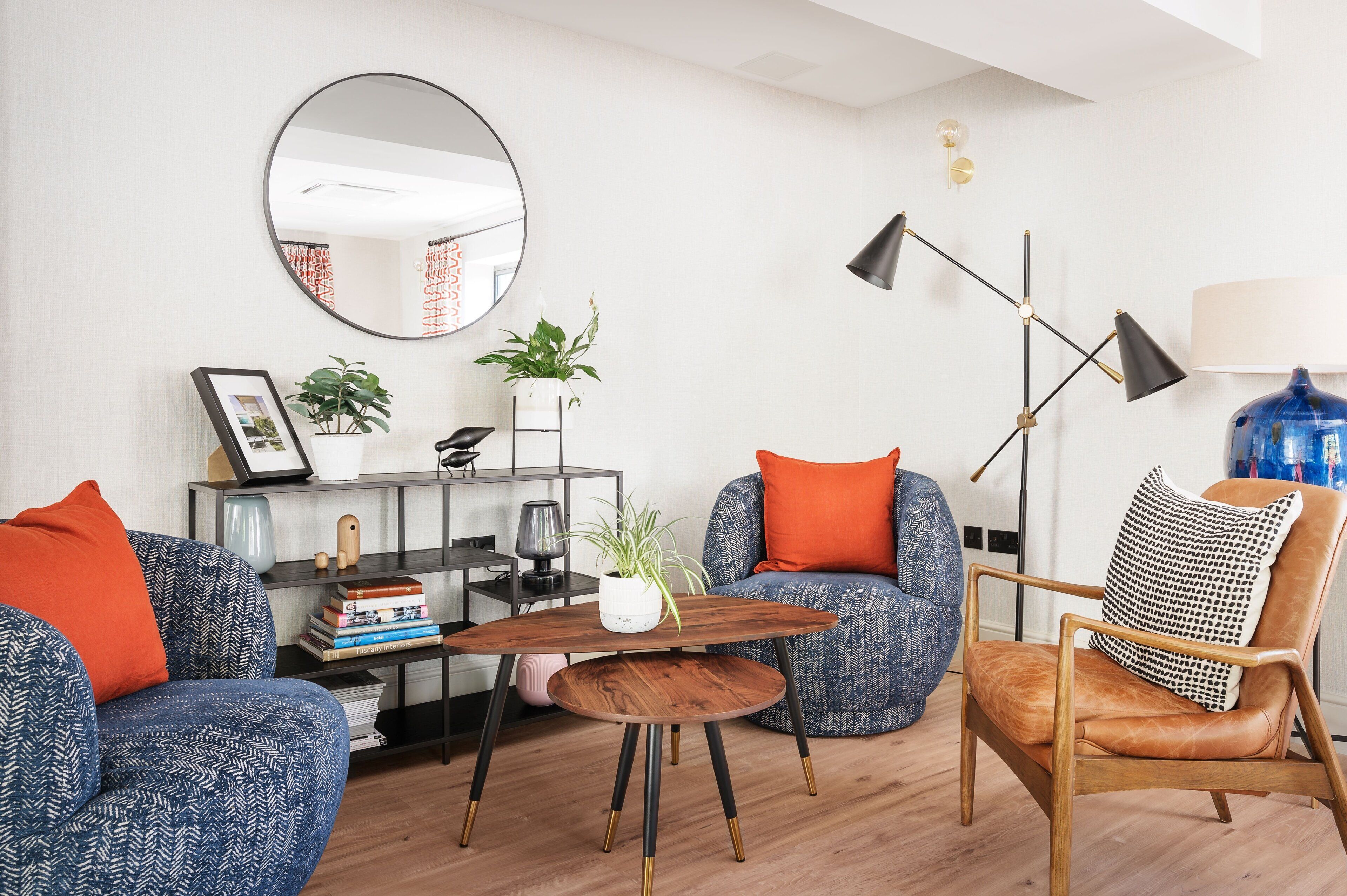 Un salon moderne avec un grand miroir rond, une table basse en bois et deux canapés bleus à motifs, agrémentés de coussins orange.