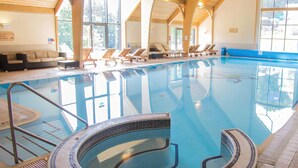 Una piscina interior con borde de azulejos, sillas de descanso y techo de madera.