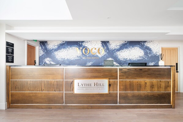 A reception desk with a wooden finish and a sign reading "LYTHE HILL HOTEL, RESTAURANT & SPA".