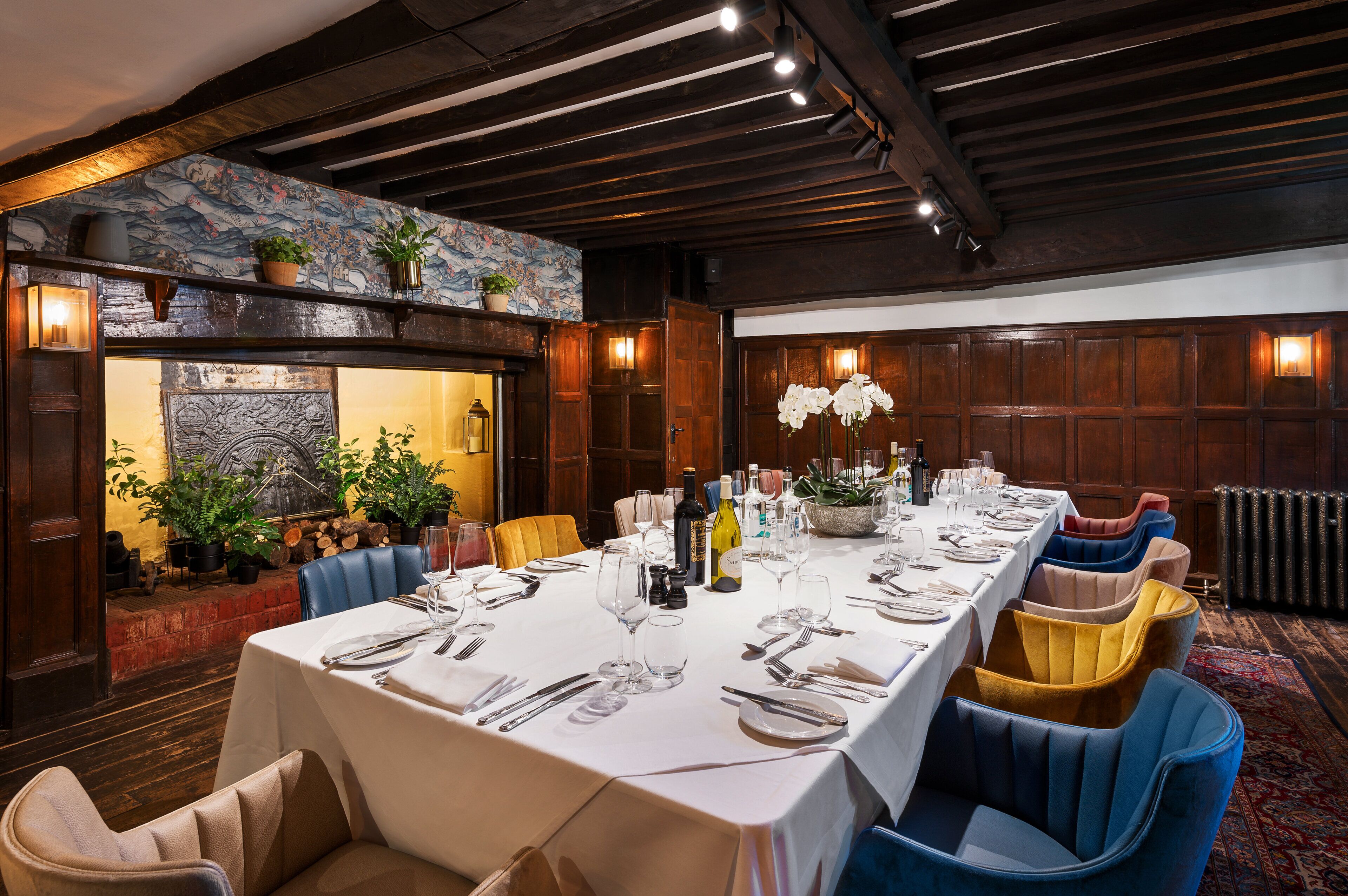 A long dining table set with white tablecloth, blue and yellow chairs, and various dining utensils.