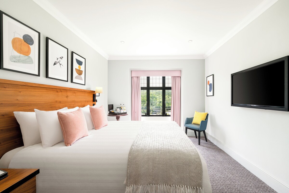 A modern hotel room with a large bed, a TV, and artwork on the walls.