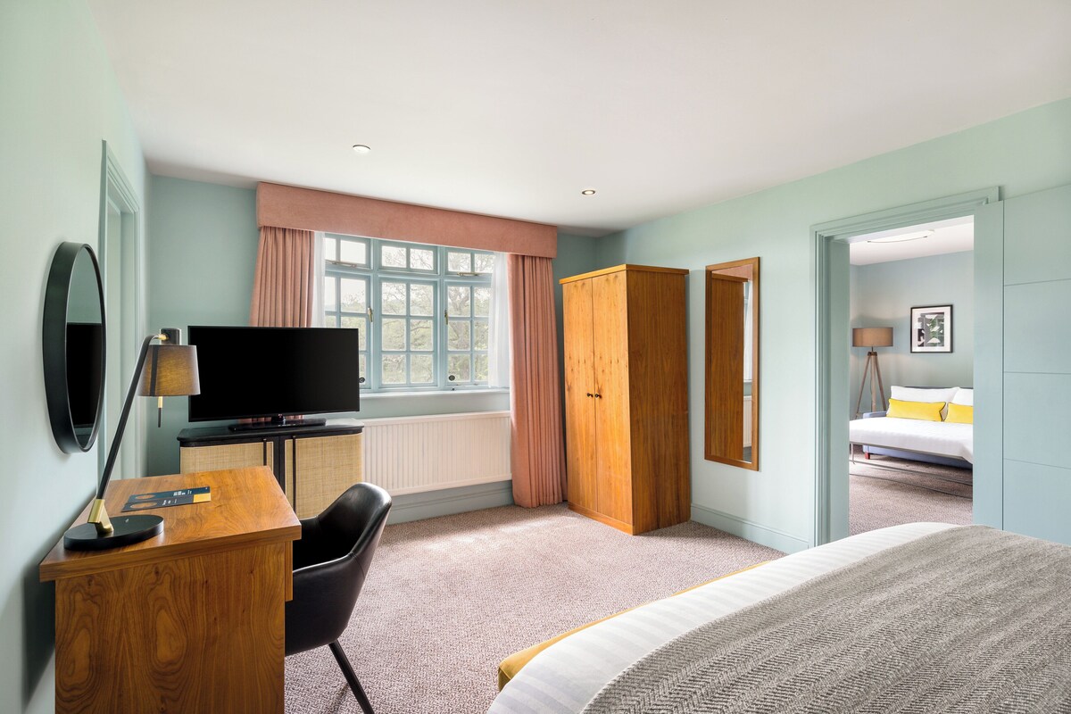 A hotel room with a bed, a desk with a TV, a wardrobe, and a window with curtains.