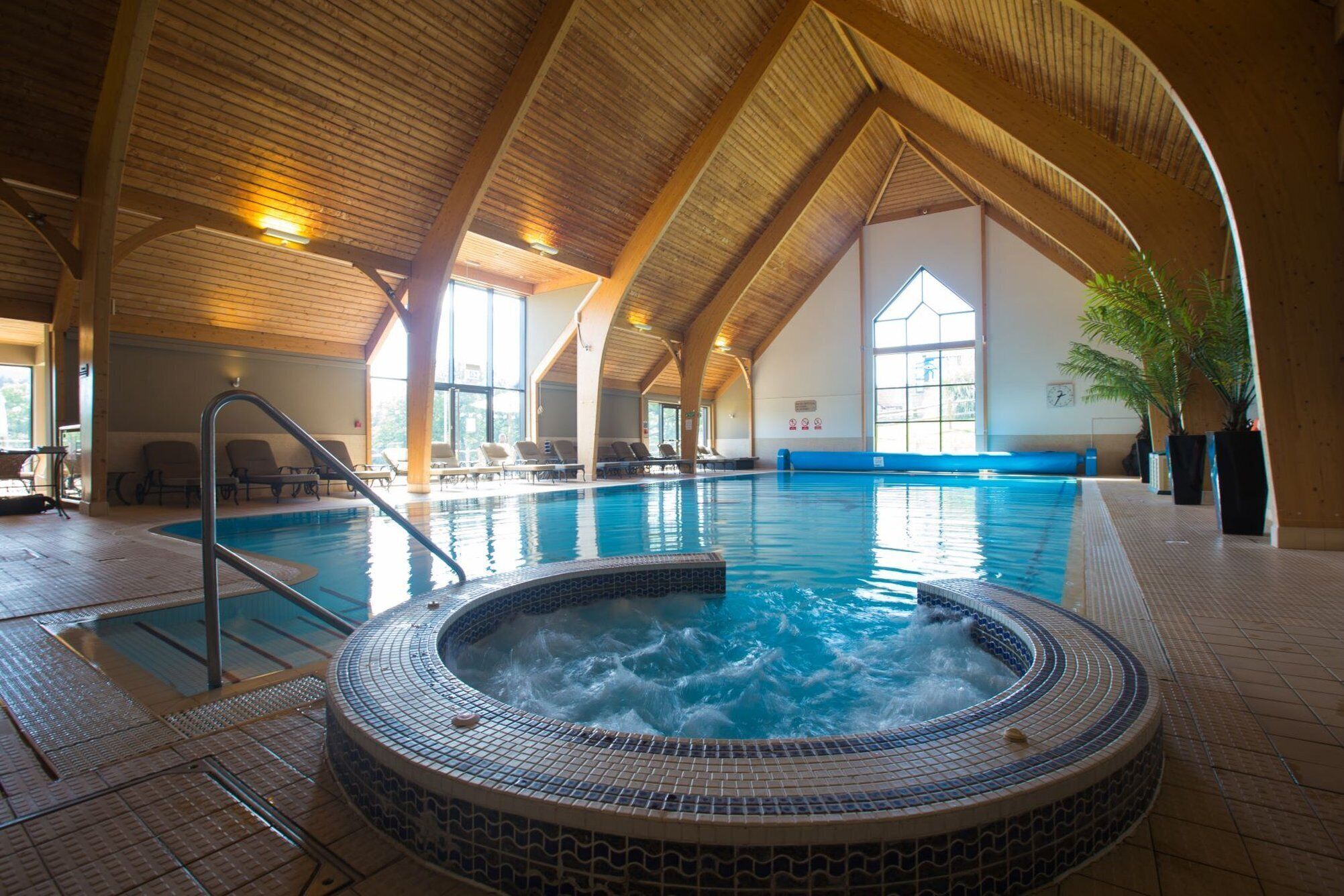 Una piscina interior con hidromasaje, sillas de descanso y techo de madera.
