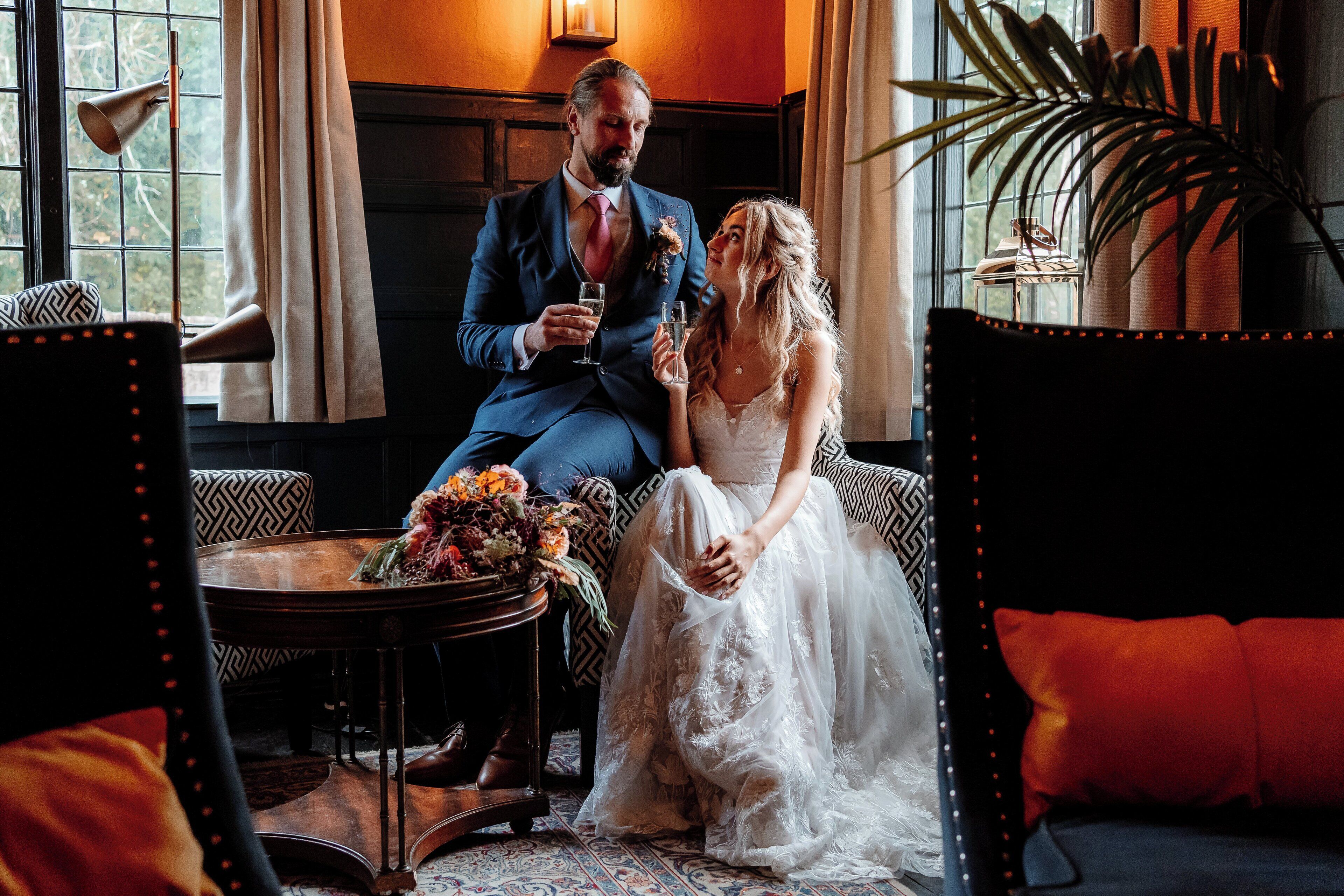 A couple seated by a window with a view, a table with flowers, and a potted plant.
