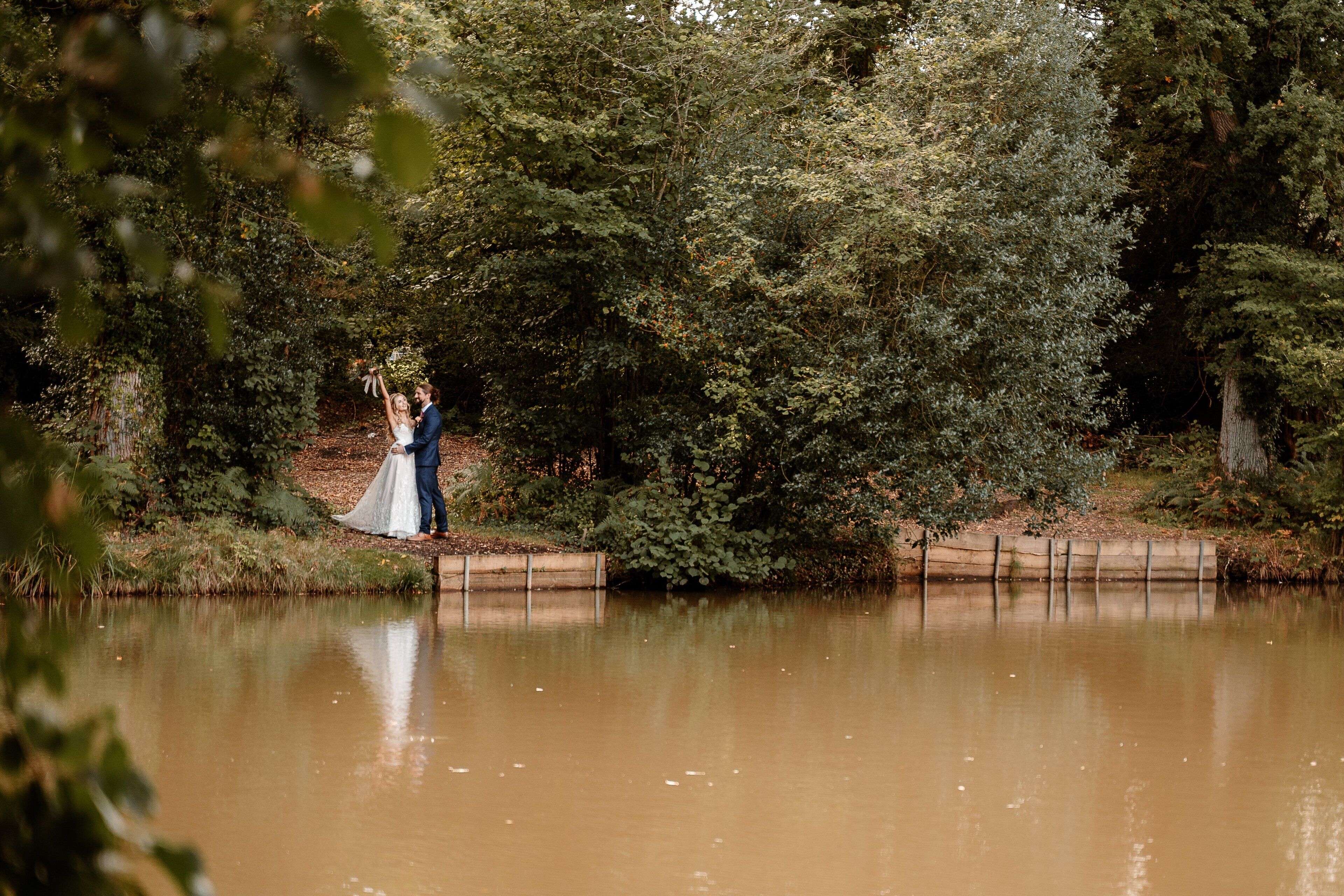 A couple standing by a calm river, surrounded by dense greenery.