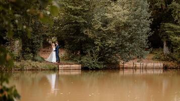 A couple standing by a calm river, surrounded by dense greenery.