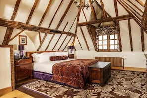 A bedroom with a wooden ceiling, a bed with a patterned bedspread, a nightstand, a dresser, a window with a view, and a radiator. - Lainston House Hotel (Winchester)