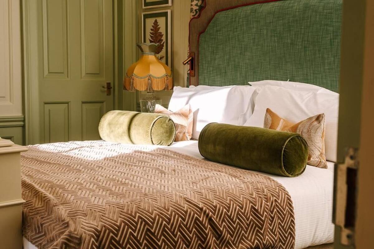 A neatly made bed with a patterned bedspread, a green cylindrical pillow, and a decorative lamp.