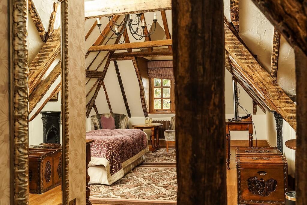 Una stanza con soffitto spiovente, un letto con copriletto decorato, un tavolino e un cassettiera.