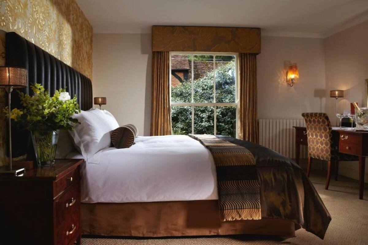 A bedroom with a bed, bedside lamps, a desk, and a window with curtains.