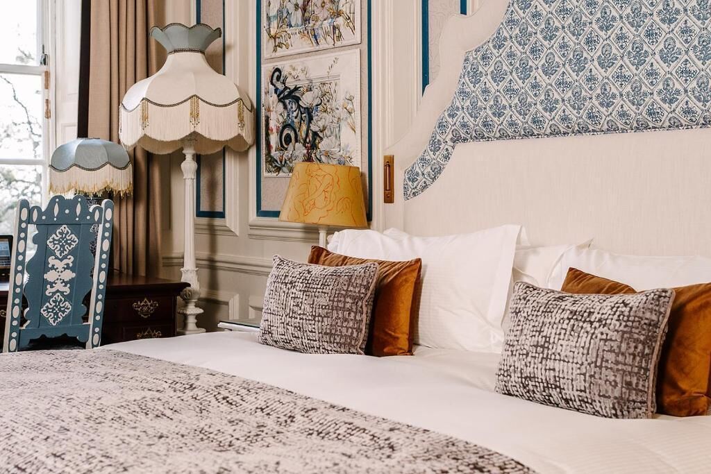Un lit bien fait, agrémenté d’oreillers à motifs, d’une lampe décorative et d’un mur orné d’œuvres d’art encadrées.