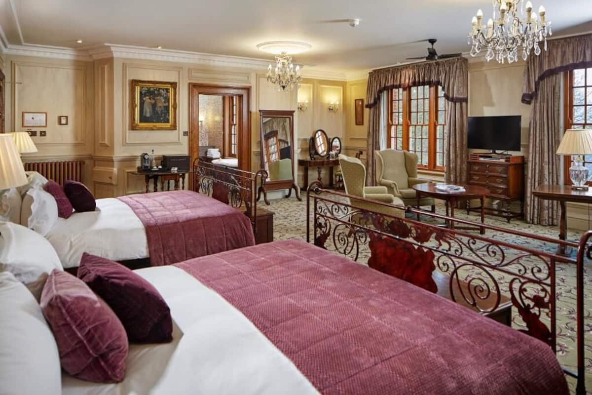 A hotel room with two beds, a desk, a television, and a chandelier.
