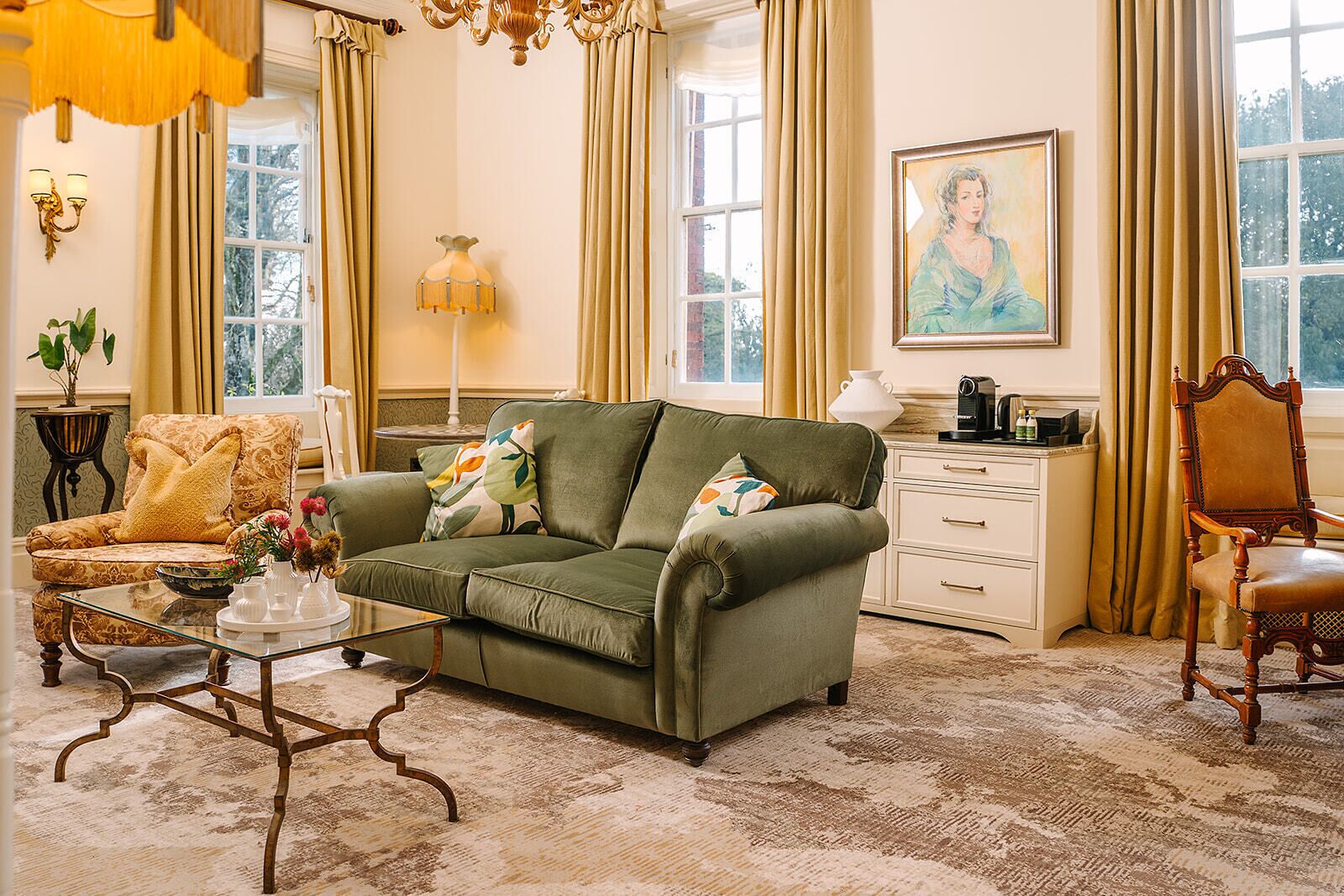 Uma sala de estar com sofá, mesa de centro, mesa lateral, abajur, poltrona e um quadro na parede.