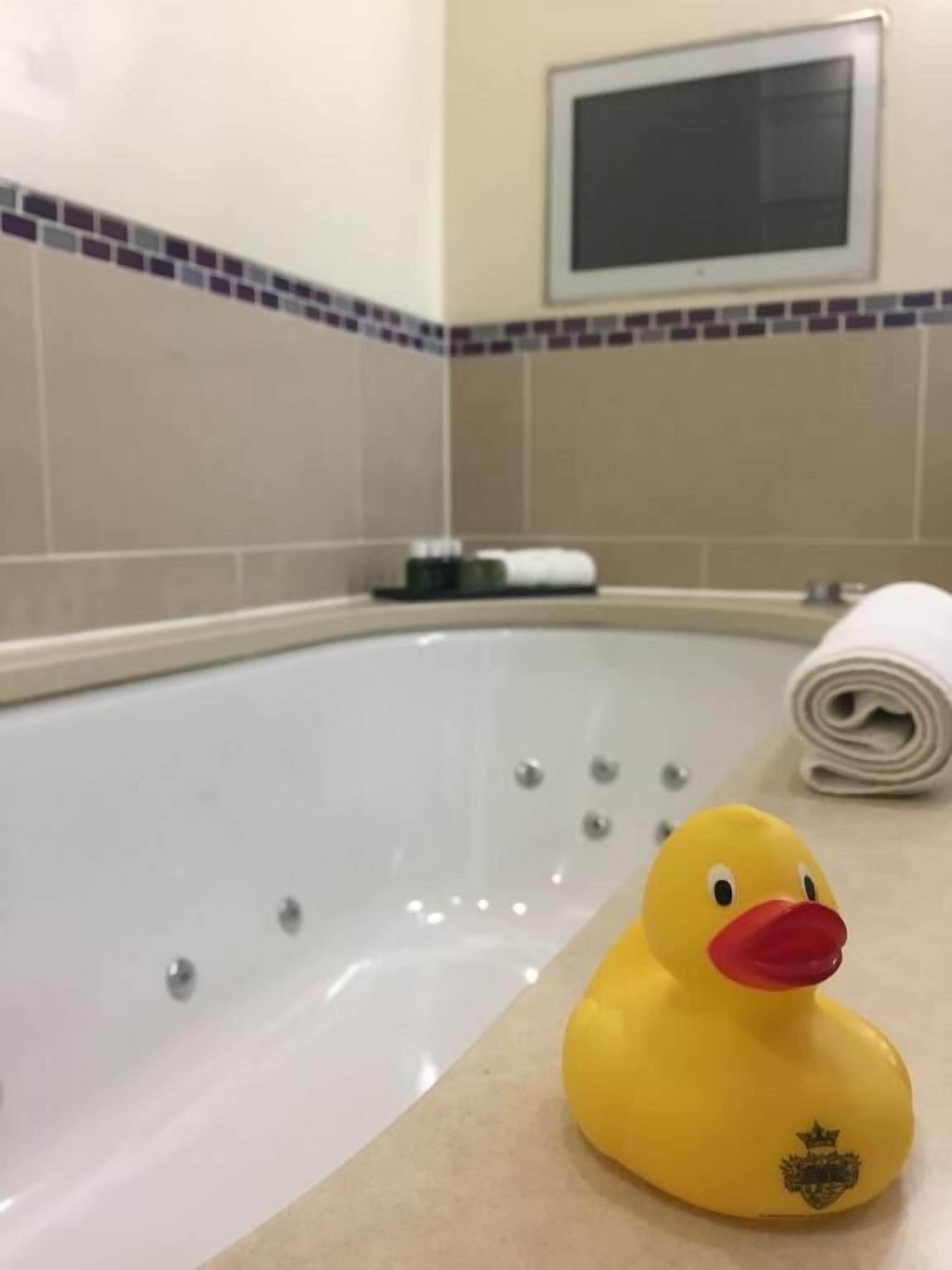 Une baignoire avec un canard en caoutchouc, une serviette et un petit écran fixé au mur.