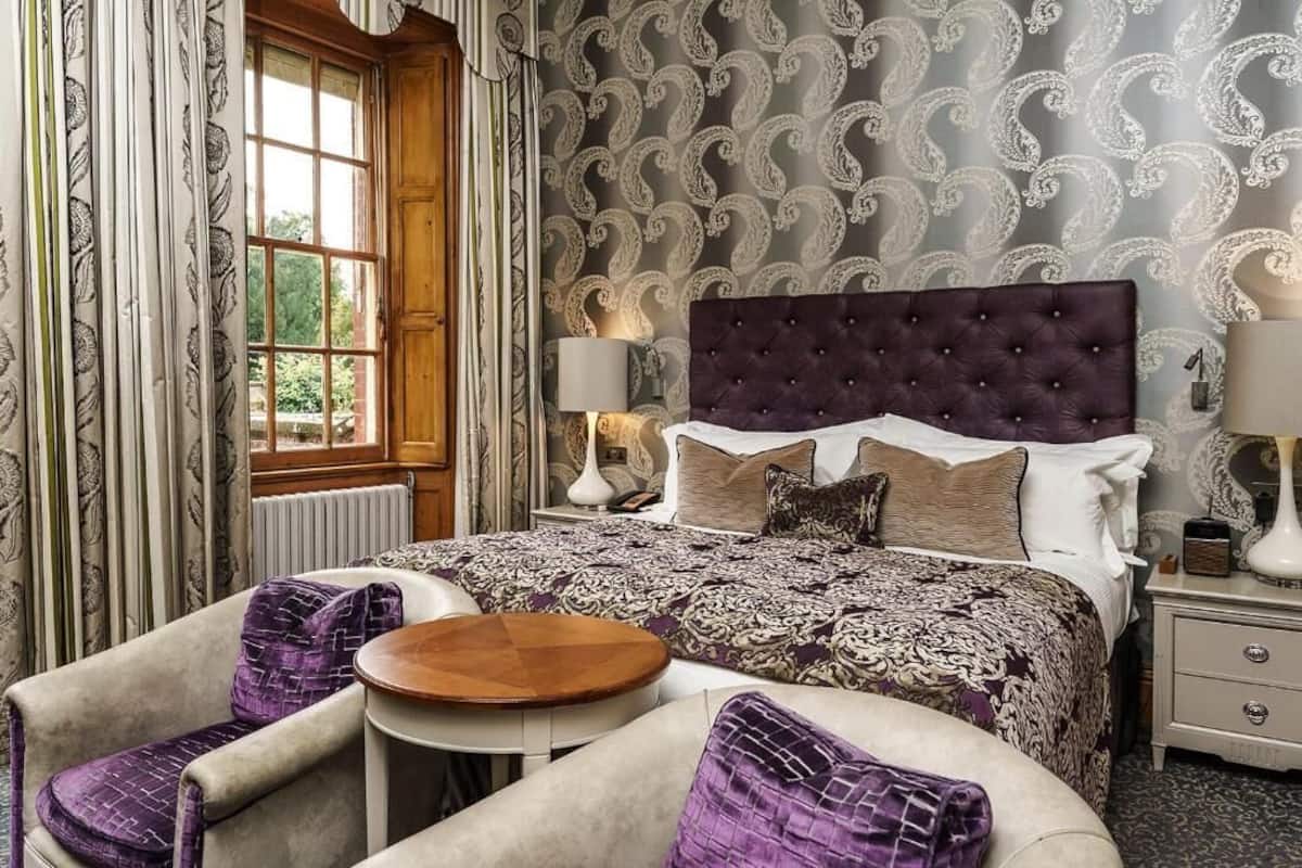 A bedroom with a large bed, two bedside tables, a round wooden table, and two armchairs.