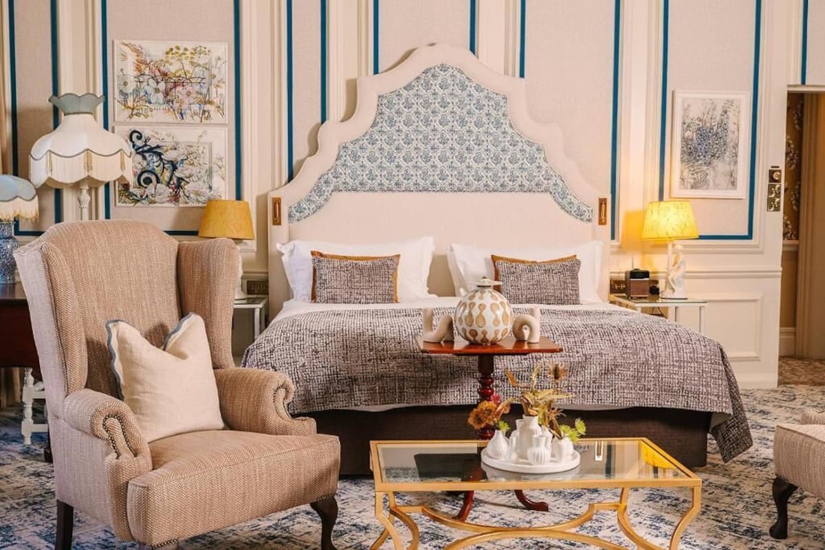 A hotel room with a large bed, a chair, a small table with a vase, and artwork on the walls.