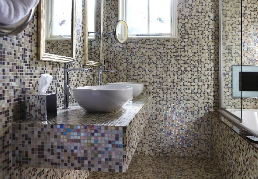 Un baño con paredes de mosaicos, un lavamanos grande de color blanco y un espejo.