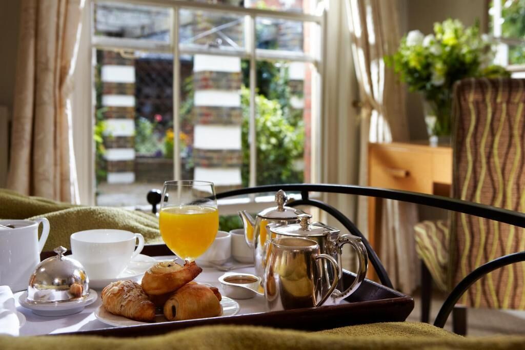 A breakfast tray with croissants, a glass of orange juice, a teapot, and a cup on a metal table.