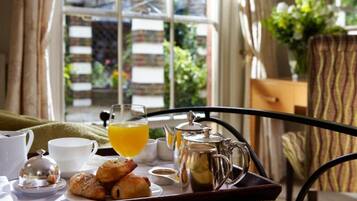 A breakfast tray with croissants, a glass of orange juice, a teapot, and a cup on a metal table.