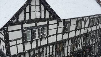 A traditional half-timbered house with snow on the roof and windows.